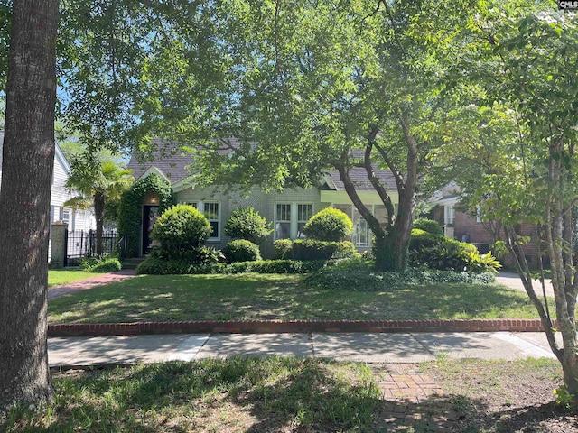 view of property hidden behind natural elements featuring fence and a front lawn