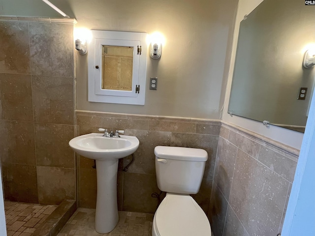 bathroom featuring wainscoting, toilet, tile walls, and a tile shower