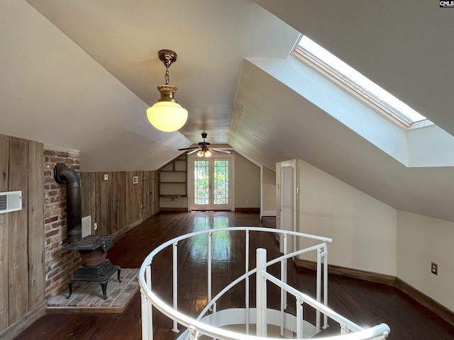 bonus room with a wood stove, hardwood / wood-style floors, baseboards, vaulted ceiling with skylight, and a ceiling fan