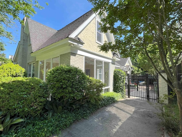 view of side of home featuring fence, a gate, a shingled roof, and brick siding