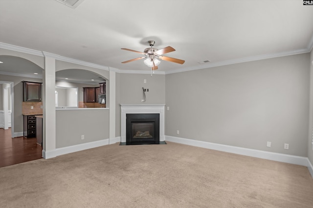 unfurnished living room featuring a ceiling fan, arched walkways, ornamental molding, and carpet