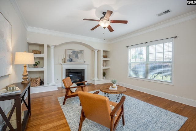 living area with a ceiling fan, visible vents, crown molding, built in shelves, and ornate columns