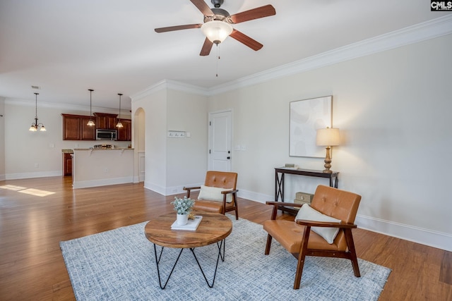 living area with arched walkways, ornamental molding, baseboards, and ceiling fan