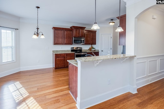 kitchen featuring appliances with stainless steel finishes, arched walkways, light wood-style flooring, a peninsula, and a kitchen bar
