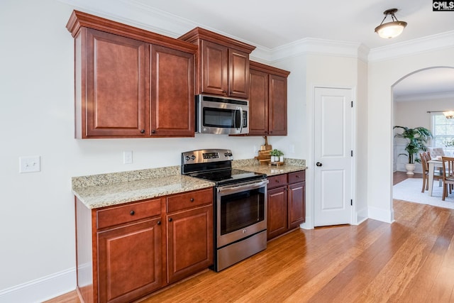 kitchen with light stone countertops, appliances with stainless steel finishes, light wood finished floors, arched walkways, and ornamental molding