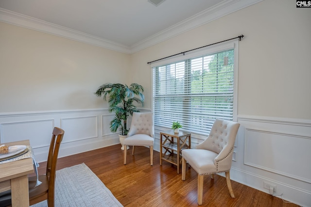 sitting room featuring ornamental molding, a decorative wall, wood finished floors, and a wainscoted wall