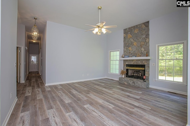 unfurnished living room with a fireplace, wood finished floors, high vaulted ceiling, baseboards, and ceiling fan with notable chandelier