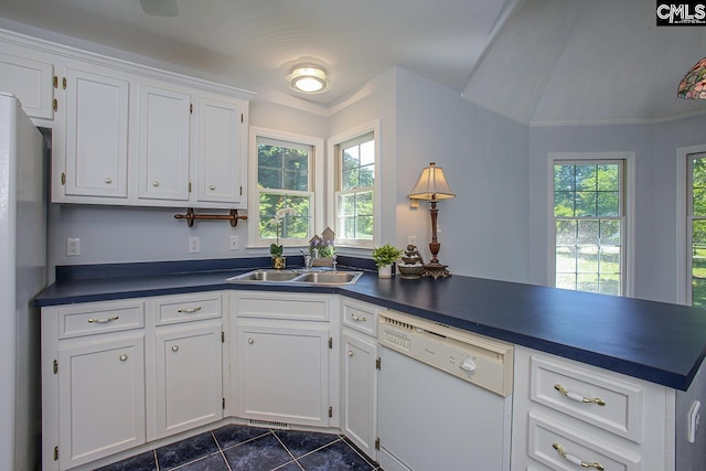 kitchen with white cabinets, dark countertops, a sink, dishwasher, and dark tile patterned floors