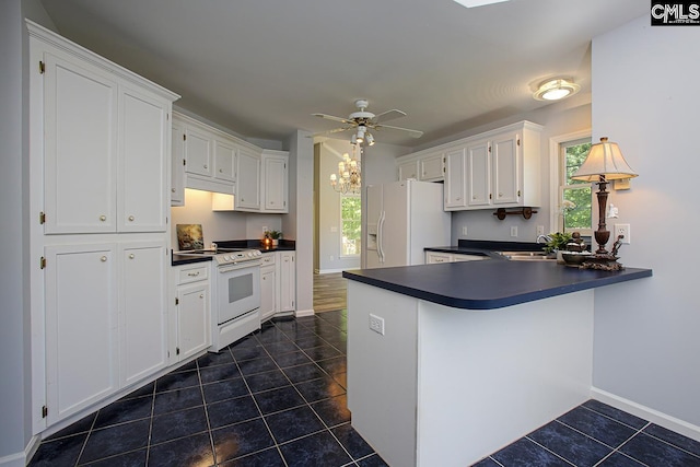 kitchen with dark countertops, dark tile patterned flooring, a peninsula, white appliances, and a wealth of natural light