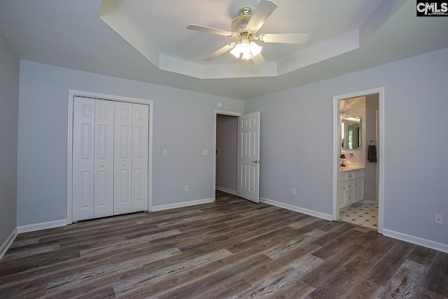 unfurnished bedroom featuring a closet, a tray ceiling, baseboards, and dark wood-type flooring