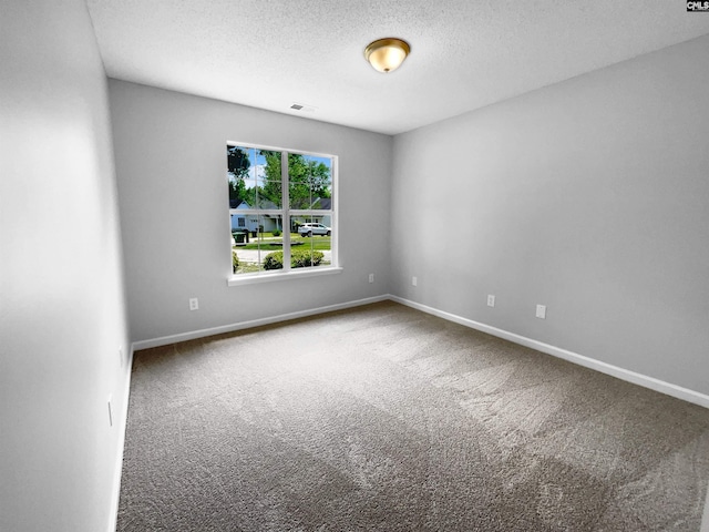 empty room with carpet flooring, a textured ceiling, baseboards, and visible vents