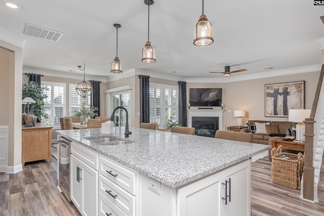 kitchen with a sink, a glass covered fireplace, light wood-style flooring, visible vents, and ornamental molding