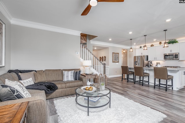 living area featuring crown molding, a ceiling fan, stairs, and wood finished floors