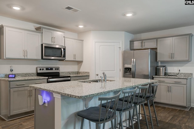 kitchen with dark wood-style flooring, appliances with stainless steel finishes, a sink, a kitchen breakfast bar, and gray cabinetry