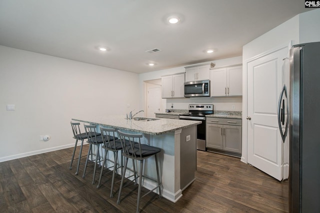 kitchen with dark wood-style flooring, appliances with stainless steel finishes, a breakfast bar, a sink, and a kitchen island with sink