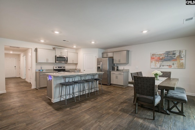 interior space with a kitchen bar, visible vents, a center island with sink, dark wood finished floors, and stainless steel appliances