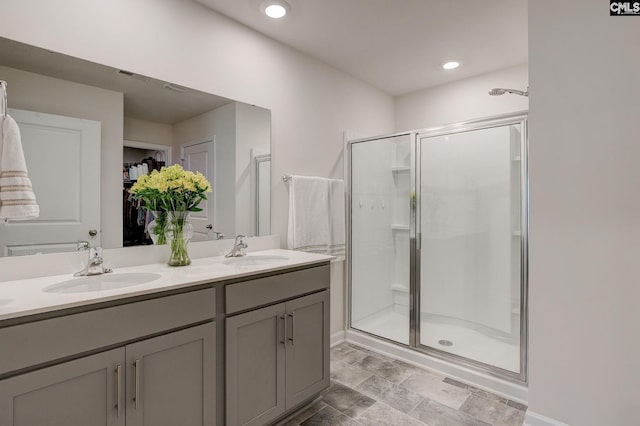 full bathroom featuring double vanity, a spacious closet, a shower stall, and a sink