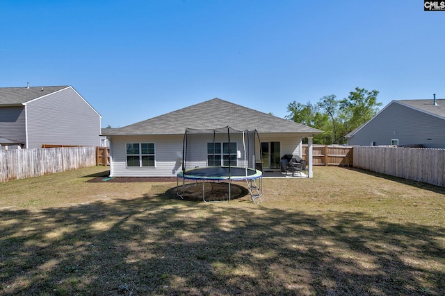 back of property featuring a fenced backyard, a trampoline, a shingled roof, and a lawn