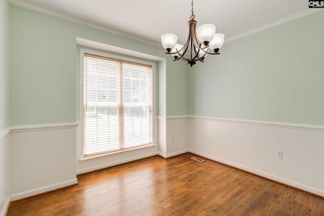 unfurnished room featuring crown molding, an inviting chandelier, plenty of natural light, and wood finished floors