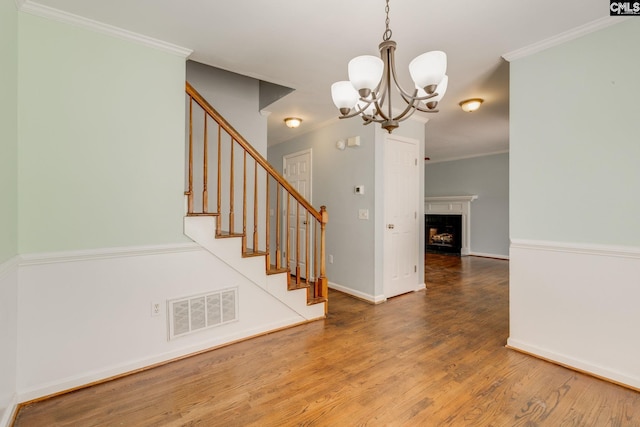 interior space with visible vents, ornamental molding, wood finished floors, baseboards, and a notable chandelier