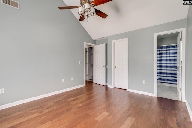 unfurnished bedroom with visible vents, wood finished floors, baseboards, high vaulted ceiling, and connected bathroom