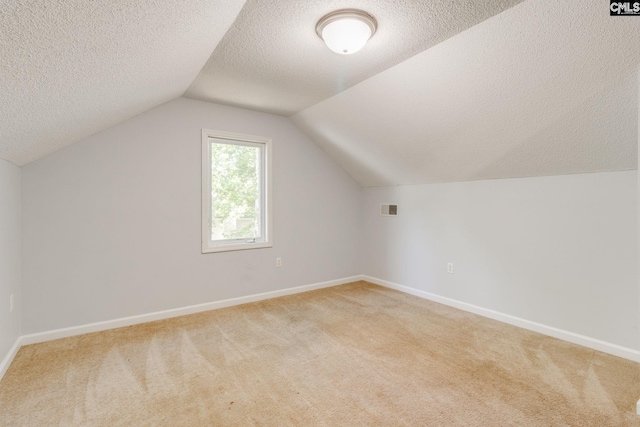 additional living space featuring visible vents, a textured ceiling, baseboards, and light carpet