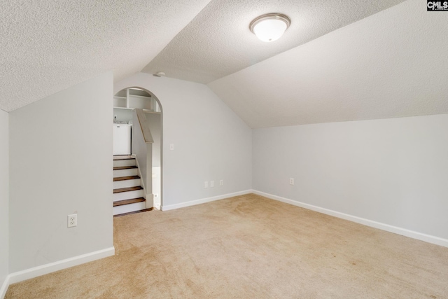 additional living space with carpet floors, stairs, baseboards, a textured ceiling, and vaulted ceiling