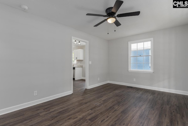 spare room featuring baseboards, ceiling fan, and dark wood-style floors