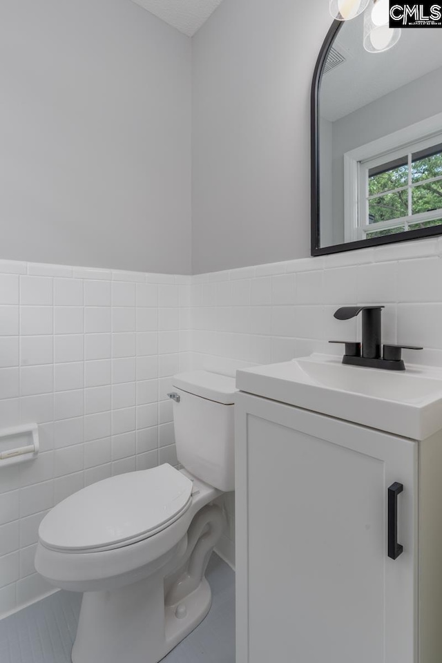 half bathroom with wainscoting, tile walls, vanity, and toilet