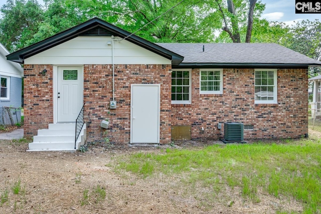 rear view of house with entry steps, central air condition unit, roof with shingles, and brick siding