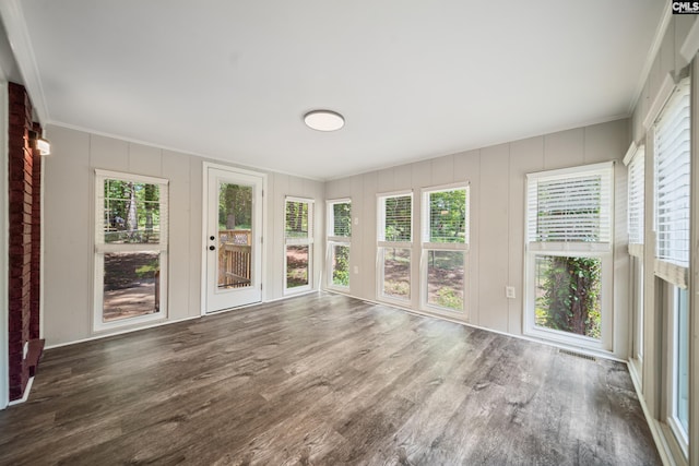 unfurnished sunroom with ornamental molding, a decorative wall, wood finished floors, and visible vents