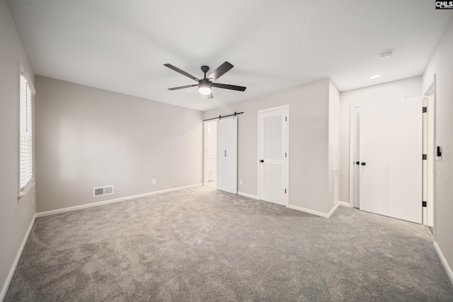 unfurnished bedroom with a ceiling fan, visible vents, a barn door, baseboards, and carpet flooring