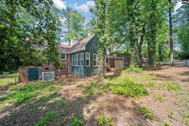 rear view of house with brick siding, fence, a chimney, and cooling unit