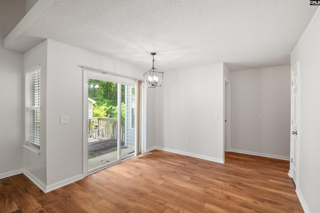 unfurnished dining area featuring a textured ceiling, wood finished floors, and a chandelier