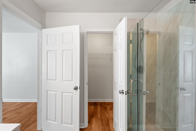 bathroom featuring a spacious closet, a shower stall, and wood finished floors