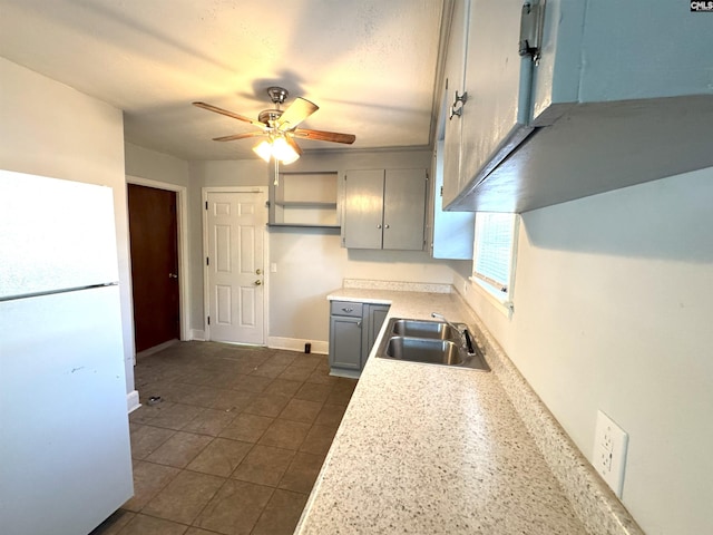 kitchen featuring gray cabinets, a ceiling fan, a sink, light countertops, and freestanding refrigerator