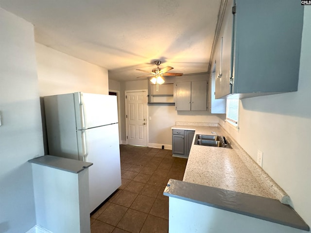 kitchen featuring ceiling fan, a sink, baseboards, dark tile patterned flooring, and freestanding refrigerator