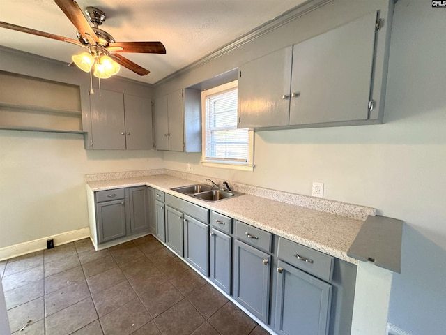 kitchen featuring a ceiling fan, baseboards, light countertops, gray cabinets, and a sink