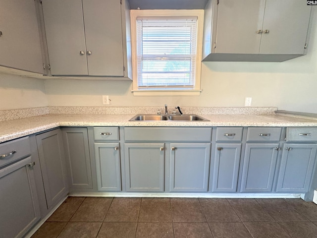 kitchen with light countertops, a sink, gray cabinetry, and dark tile patterned flooring