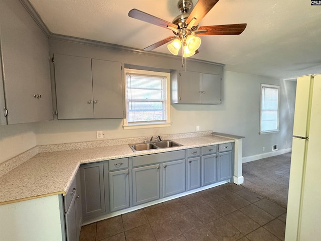 kitchen with freestanding refrigerator, ceiling fan, light countertops, dark tile patterned flooring, and a sink