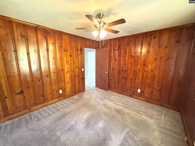 carpeted spare room with a ceiling fan and wood walls