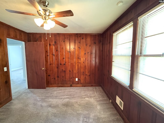 unfurnished room with wooden walls, a ceiling fan, visible vents, and carpet