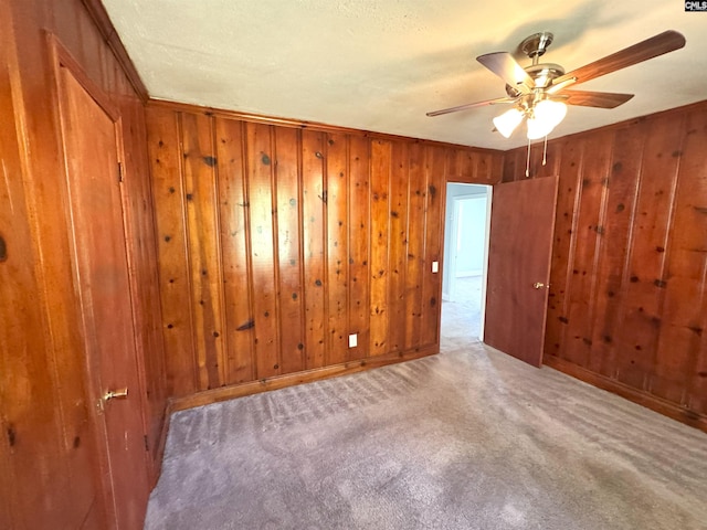 carpeted empty room with wood walls and ceiling fan