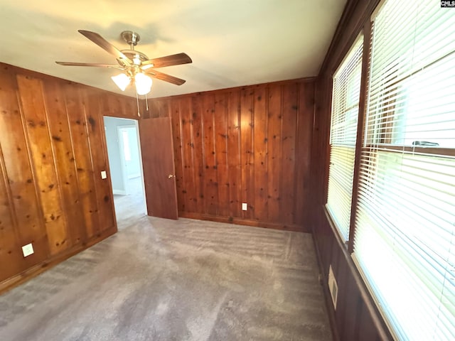 carpeted spare room with wooden walls and ceiling fan