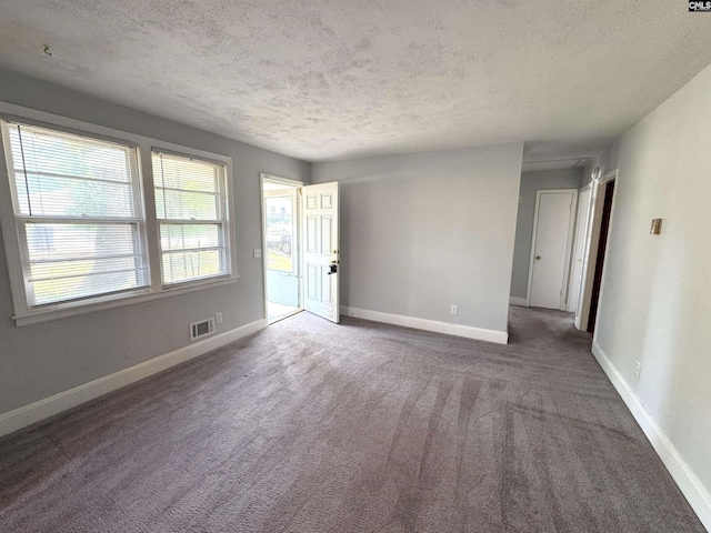 carpeted spare room featuring a textured ceiling, visible vents, and baseboards