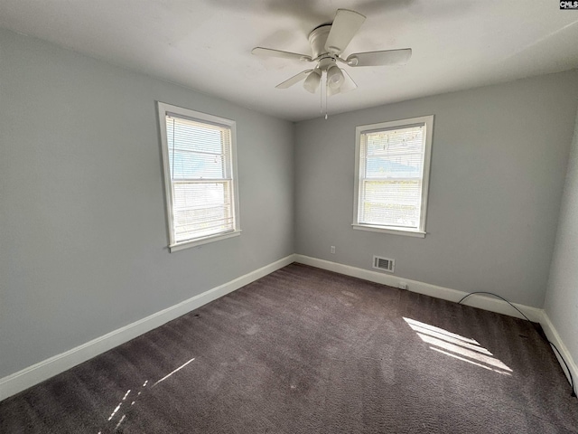 spare room with dark colored carpet, a ceiling fan, baseboards, and visible vents