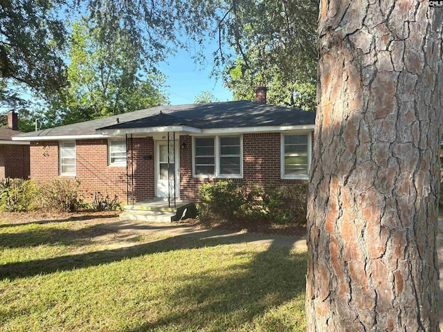single story home with brick siding, a front lawn, and a chimney