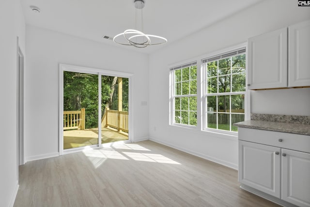 unfurnished dining area featuring baseboards, light wood finished floors, a chandelier, and visible vents