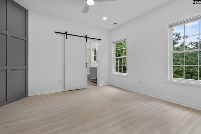 unfurnished bedroom with visible vents, a barn door, light wood-style flooring, and multiple windows