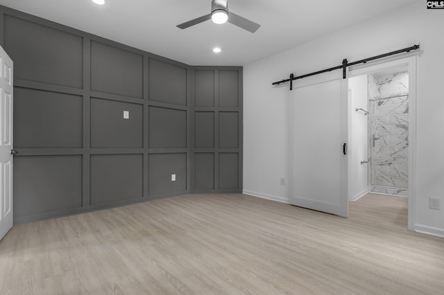 interior space featuring a decorative wall, baseboards, ceiling fan, a barn door, and light wood-style flooring